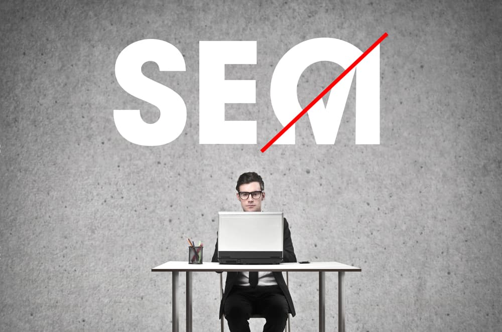 a big text of seo and sem with a man sitting on a table with a laptop