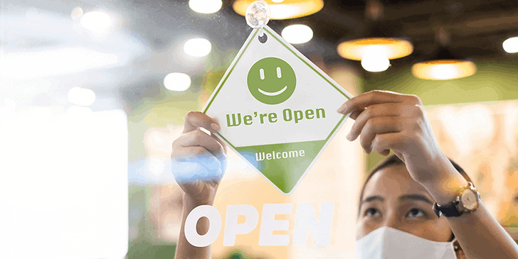 women putting a we're open and welcome sign